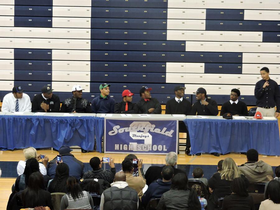 Senior Jeremy Gates (standing) announces that he is signing to play football for Saginaw Valley State University. Gates fellow football players smile proudly as they listen to him.